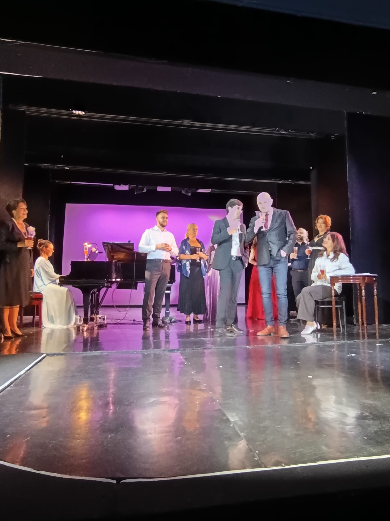 Mehrere Personen feiern auf einer Bühne in einer Theateraufführung.